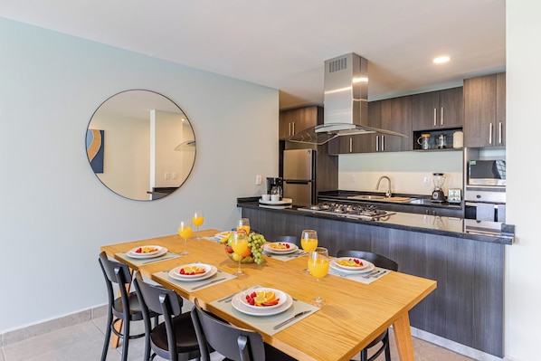 A modern kitchen with a central island, stainless steel appliances, and a dining area with a wooden table and chairs. - Vrbo Property (Cuernavaca)