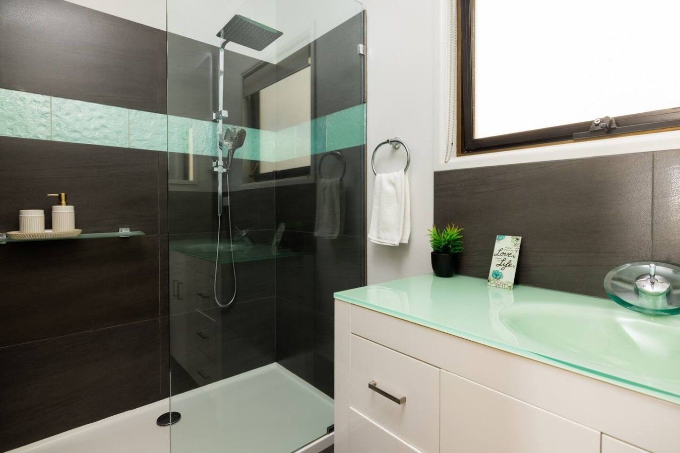 A modern bathroom with a glass-enclosed shower, a glass sink, and a white vanity.