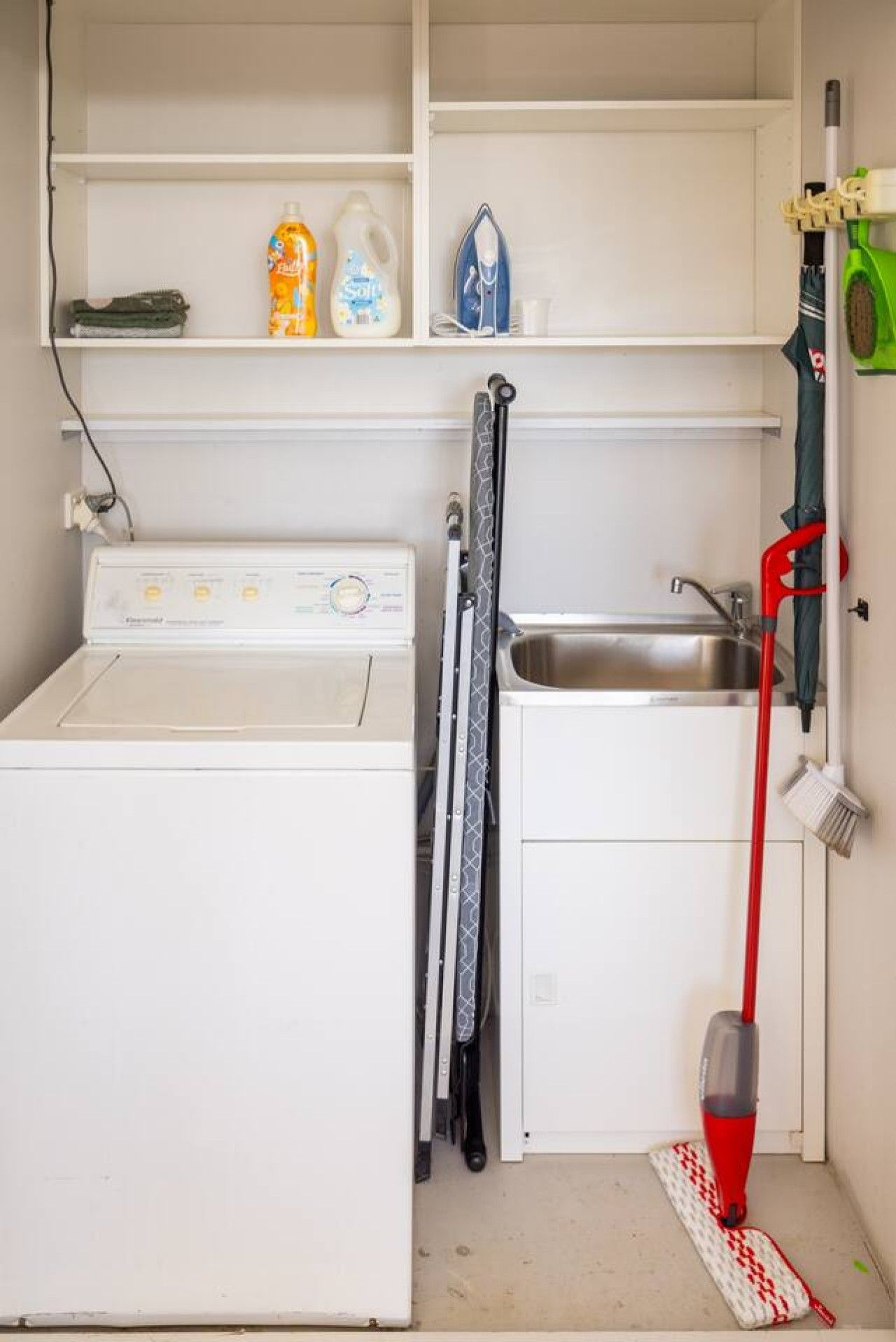 Une petite buanderie équipée d’un lave-linge, d’un évier et de divers produits de nettoyage.