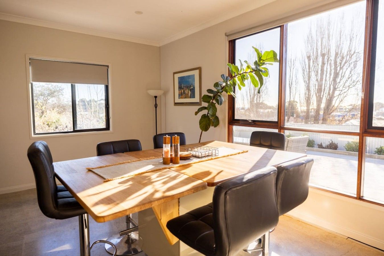 A conference room with a wooden table, black chairs, a potted plant, and a painting on the wall.