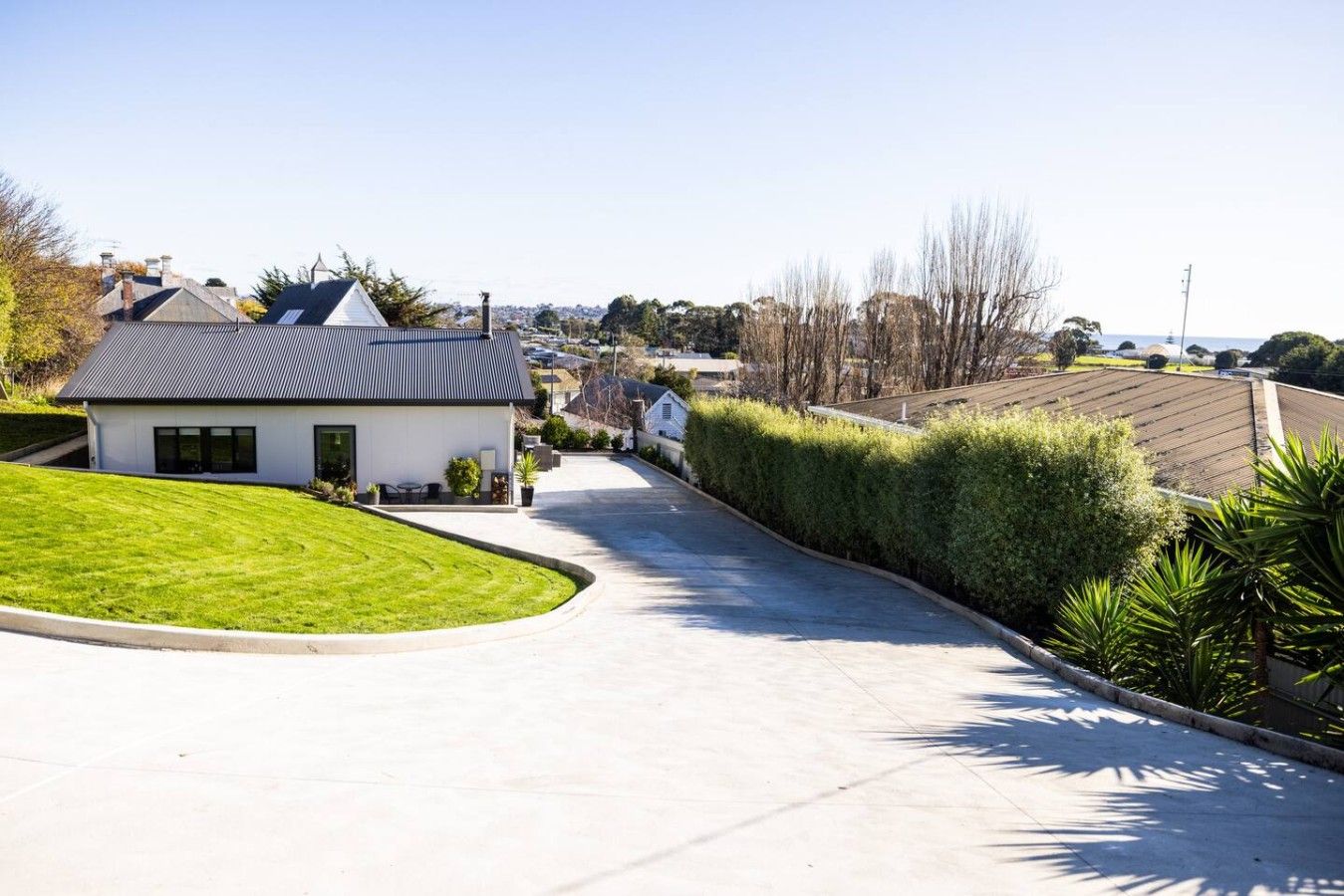 A residential street with a modern house, a well-maintained lawn, and a clear sky.