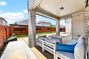 A covered outdoor patio with a fire pit, seating, and a brick wall. - *NEW* 6BR, 4 Kings, MovieRoom, BilliardS, MiniGolf (Katy)