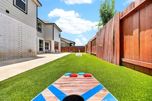 Een achtertuin met een jeu de boules baan, een houten hek en een huis met een gevel van baksteen.