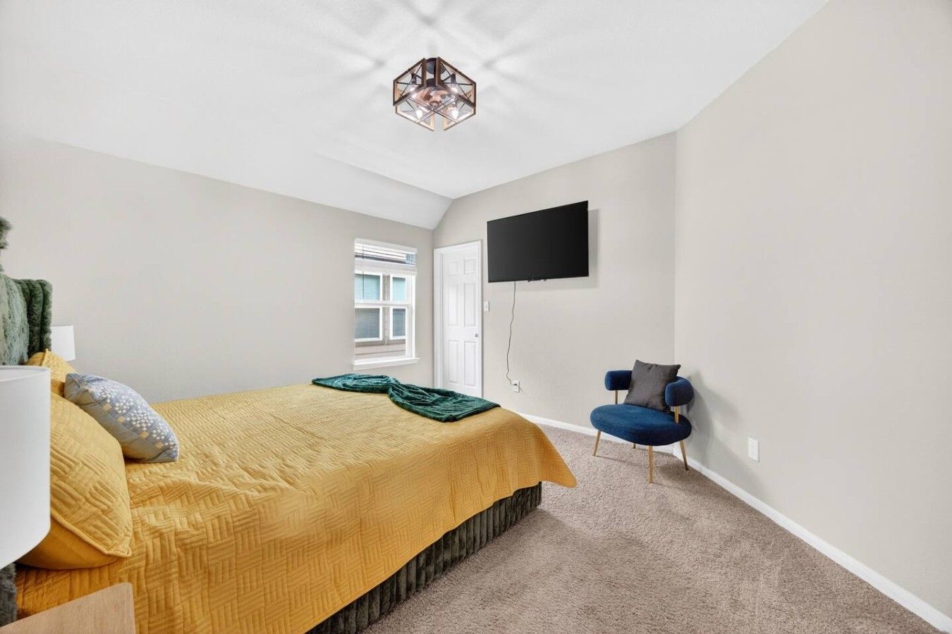 A bedroom with a bed, a chair, a television mounted on the wall, and a window.