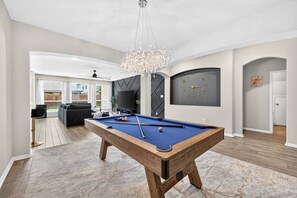 Een ruime kamer met een pooltafel, een kroonluchter, een klok en een televisie.