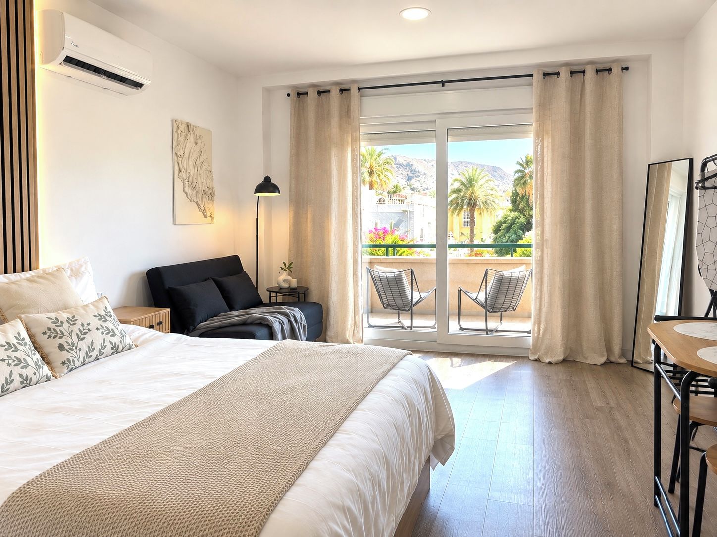 A hotel room with a bed, a desk, a chair, a balcony with a view, and an air conditioning unit.