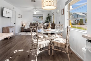 A dining area with a round glass table surrounded by wicker chairs, a ceiling fan, and a view of the outside. - Sunny Pinecraft Retreat (Sarasota)