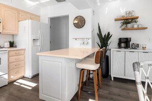 A modern kitchen with a central island, wooden cabinets, a clock, and a coffee station. - Sunny Pinecraft Retreat (Sarasota)