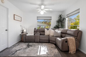 A modern living room with a sectional sofa, a ceiling fan, a large window, and a potted plant. - Sunny Pinecraft Retreat (Sarasota)