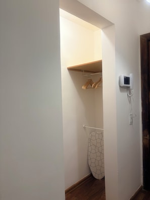 Ein Flur mit Holzboden, einem Kleiderständer, einem aufgehängten Kleidungsstück und einem an der Wand befestigten Telefon.