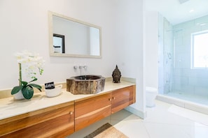 A bathroom with a wooden vanity, a round sink, a mirror, a shower area, and a small plant. - Ideally situated in the heart of town and a 4 min walk to the Beach. (Tamarindo)