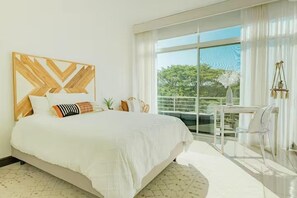 A modern hotel room with a large bed, a wooden headboard, a balcony with a view, and a small table with chairs. - Reserve Costa Rica - 3 Bed - ocean view condo Tamarindo (Tamarindo)