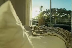 A bed with a blanket and a pillow, a window with a view of trees and a balcony. - Reserve Costa Rica - 3 Bed - ocean view condo Tamarindo (Tamarindo)