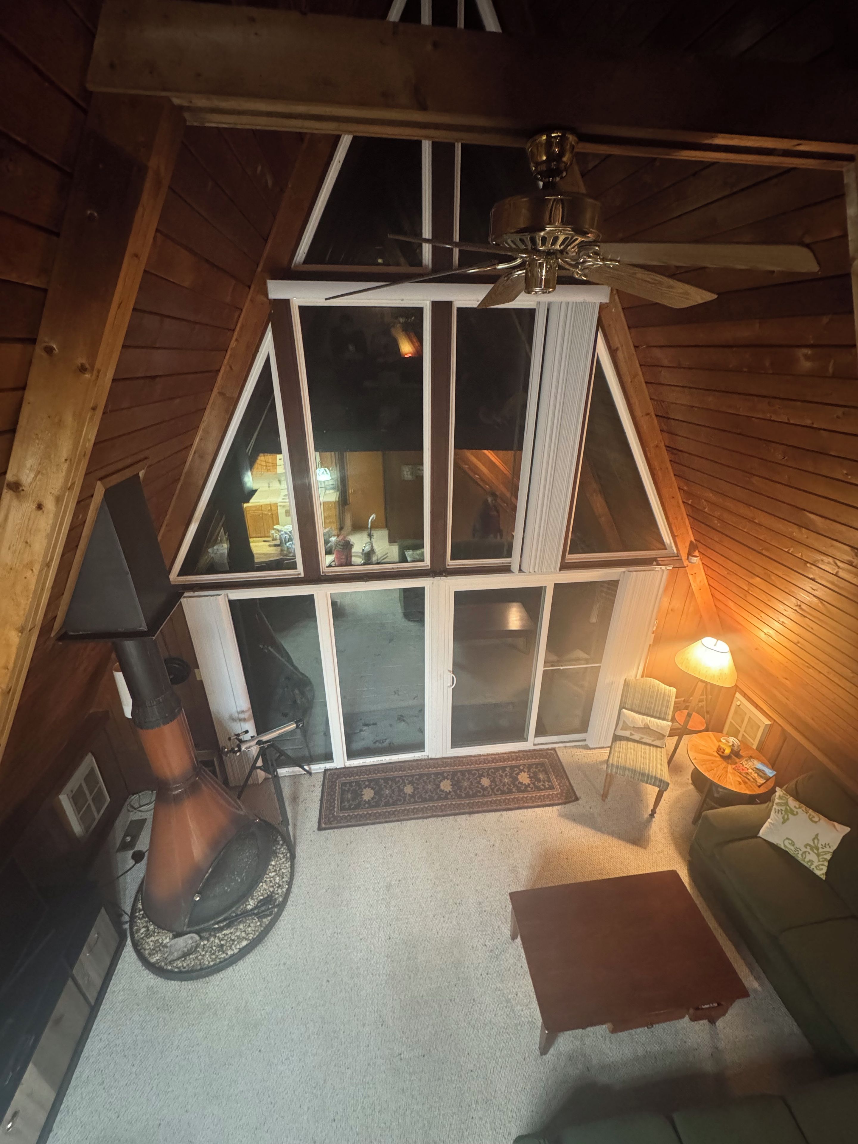 Ein gemütliches Schlafzimmer im Dachgeschoss mit schrägen Wänden, einem Deckenventilator, einem Kamin, einer Couch, einem Couchtisch und einem Fenster mit Blick ins Innere.
