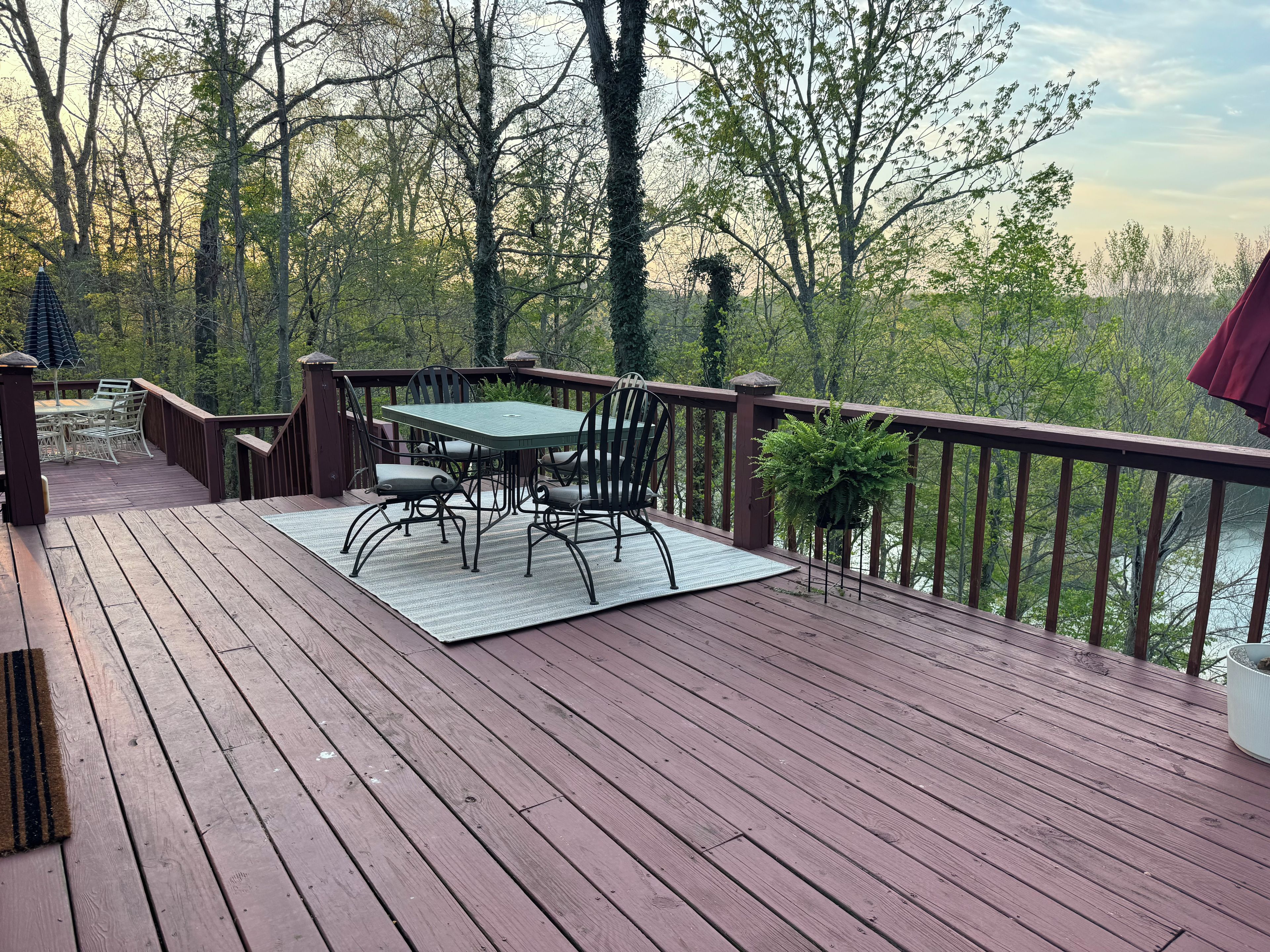 A wooden deck with a table and chairs, surrounded by trees and overlooking a body of water.