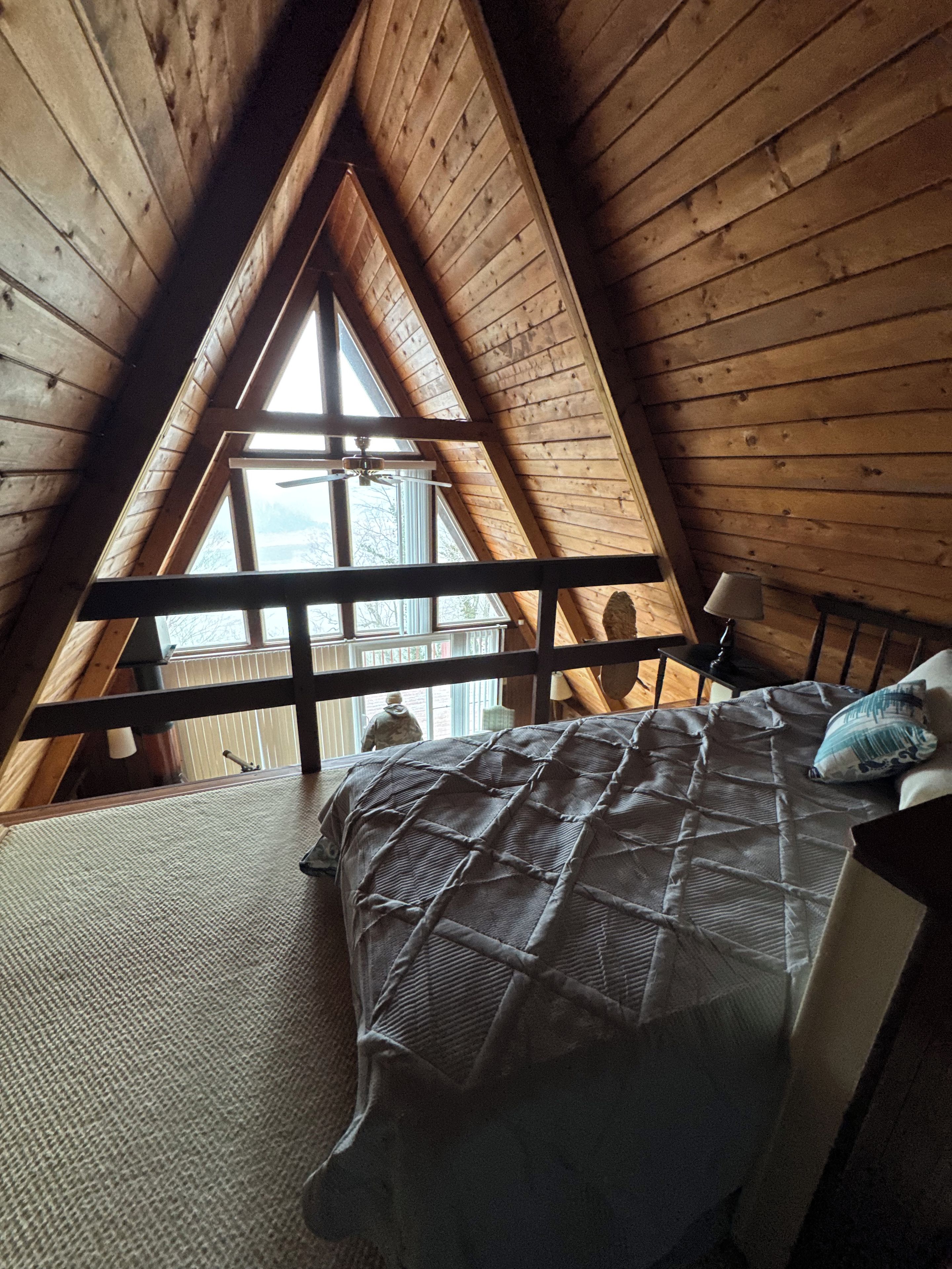 Une chambre avec un plafond en pente, un lit recouvert d’une couvre-lit à motifs, une table de chevet et une fenêtre donnant sur l’extérieur.