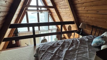 Une chambre avec un plafond en pente, un lit recouvert d’une couvre-lit à motifs, une table de chevet et une fenêtre donnant sur l’extérieur.