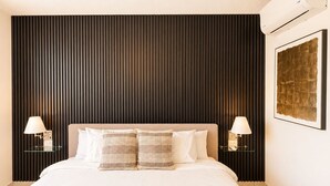 Une chambre d’hôtel avec un grand lit, deux lampes de chevet, un climatiseur fixé au mur et une œuvre d’art encadrée accrochée au mur.