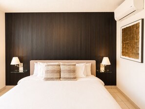 A hotel room with a large bed, two bedside lamps, a wall-mounted air conditioner, and a framed artwork on the wall. - Vrbo Property (San Salvador)