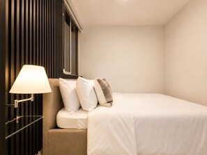 A hotel room with a bed, a bedside lamp, and a wall-mounted light fixture.