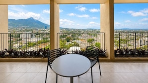Un balcon avec une table ronde et deux chaises, d’où l’on peut admirer un panorama urbain avec des montagnes et des immeubles.