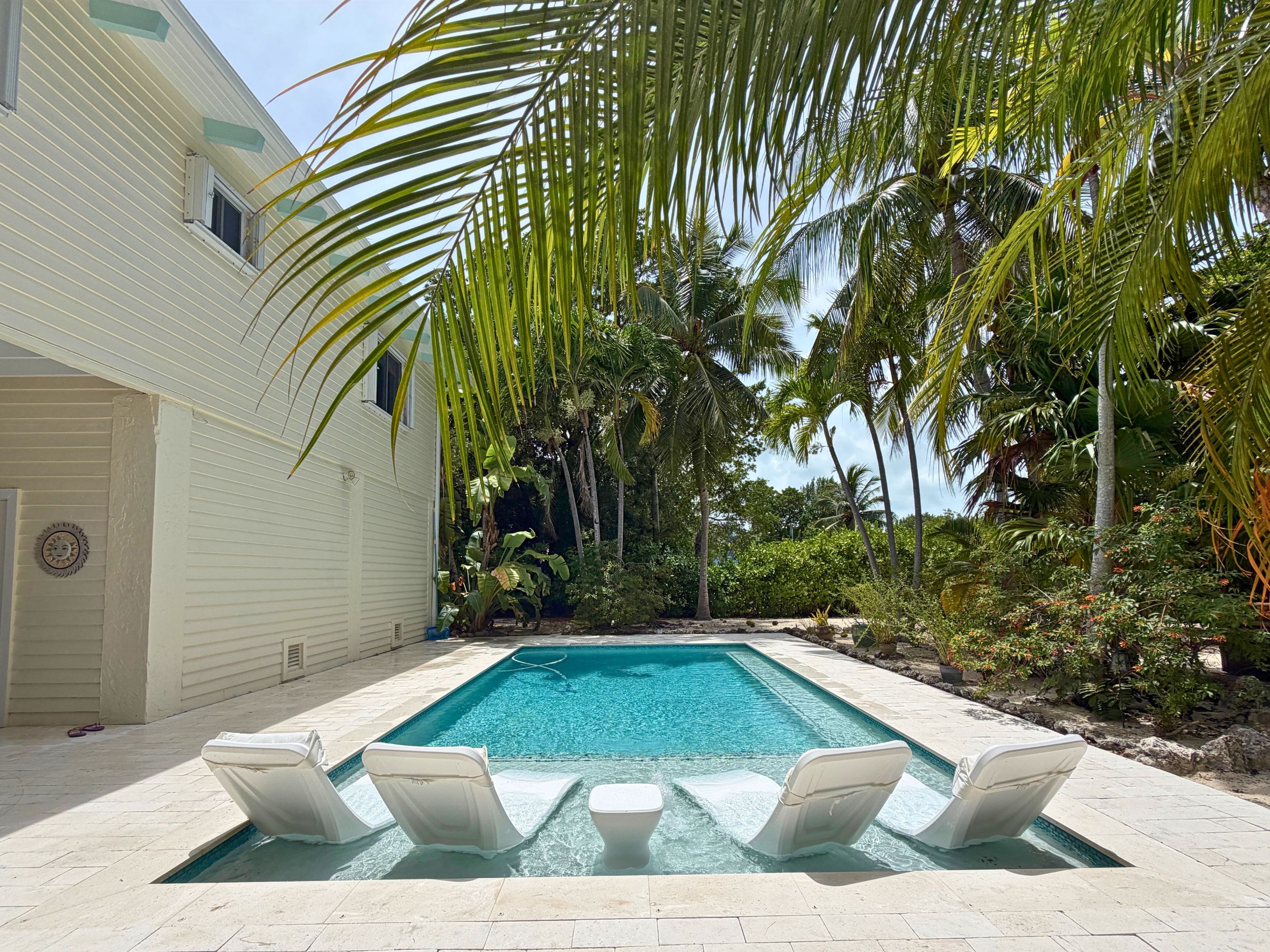 A swimming pool with lounge chairs, surrounded by palm trees and a white building.