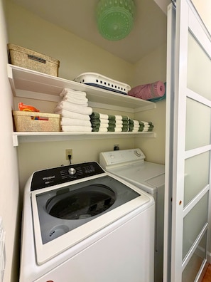 A laundry room with a front-loading washer and dryer, shelves with folded towels, and a basket. - KeyLime Oasis - Private Pool, 3 Beds, 2 Baths, with Boat Parking (Tavernier)