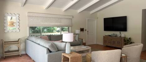 Ein Wohnzimmer mit einem grauen Sofa, einem Fernseher und einem Deckenventilator.