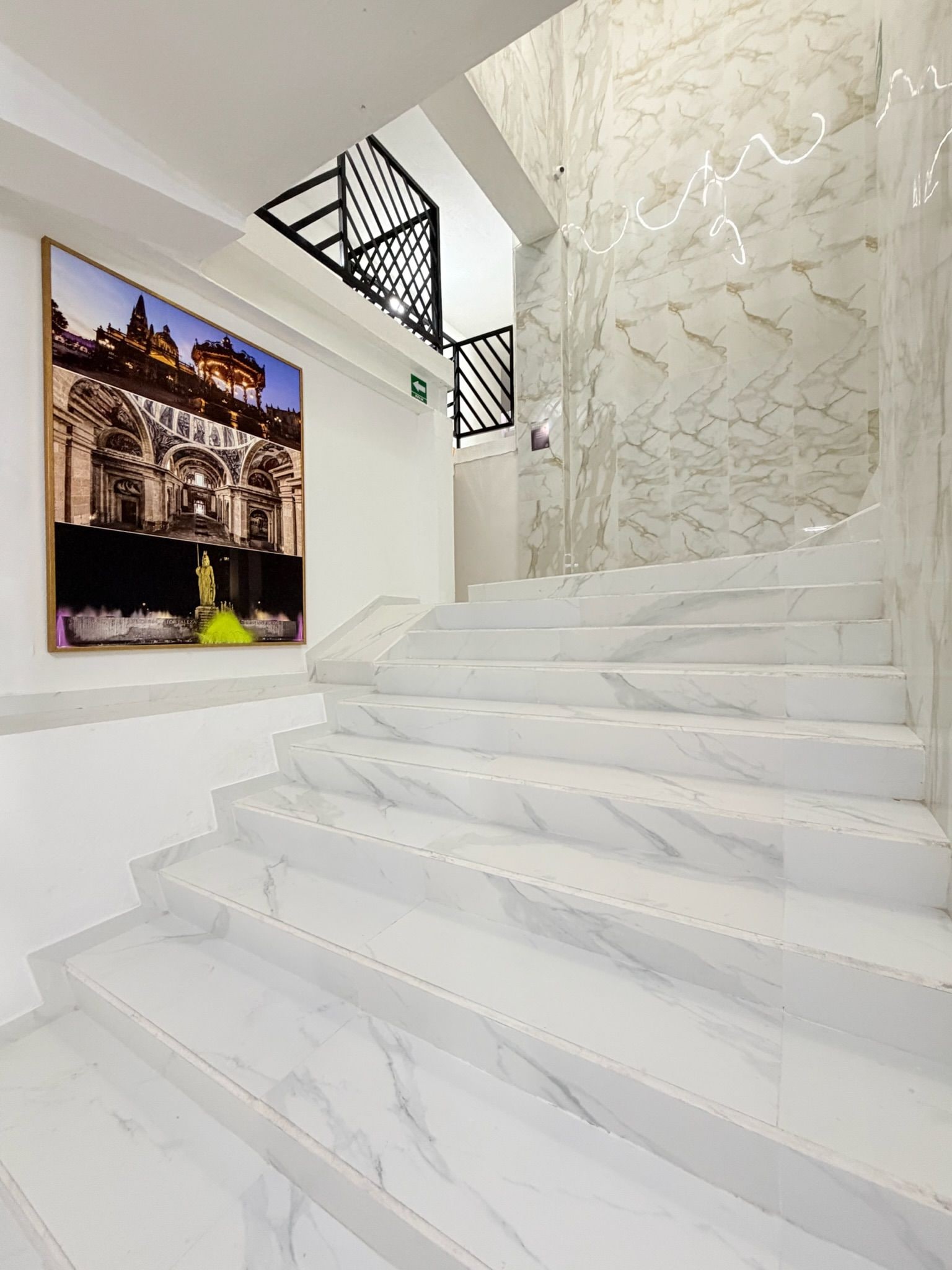 Una escalera con escalones de mármol blanco y barandilla de metal negro.