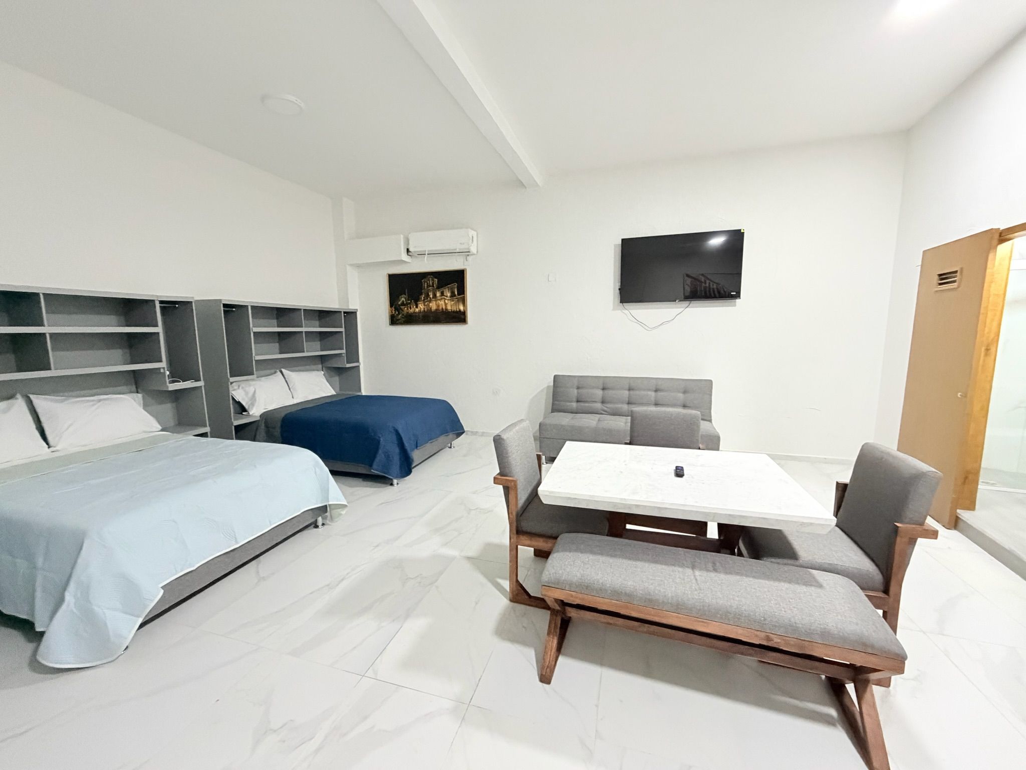 Una habitación de hotel con cama, sofá, mesa con sillas, televisor y armario.