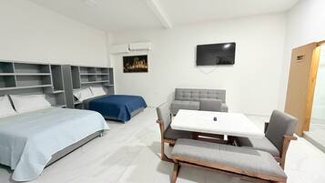 Una habitación de hotel con cama, sofá, mesa con sillas, televisor y armario.