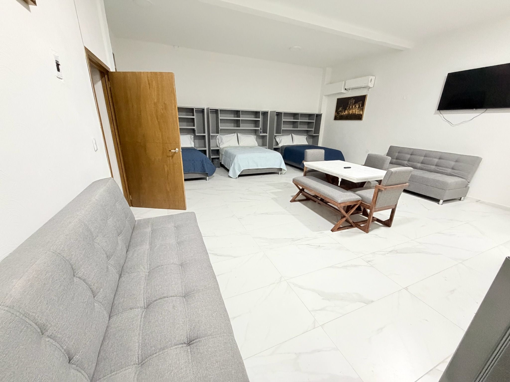 Una sala de estar moderna con un sofá gris, una mesa de comedor con sillas, un sofá gris y un televisor montado en la pared.