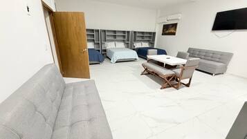 Una sala de estar moderna con un sofá gris, una mesa de comedor con sillas, un sofá gris y un televisor montado en la pared.