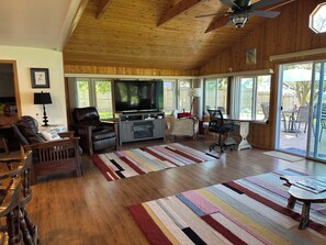 Un salón amplio con una televisión grande, techo de madera y vistas al exterior.