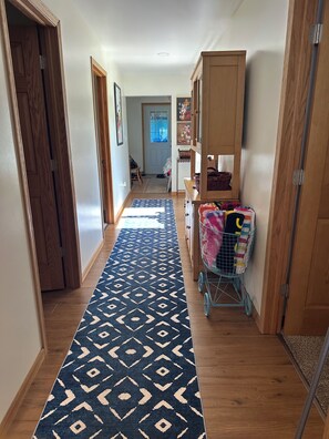Un pasillo con alfombra estampada, armarios de madera y un carro de lavandería.