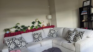 A living room with a grey sectional sofa, patterned cushions, a red and black striped side table, and a black bookshelf. - Delta room (Fort McMurray)