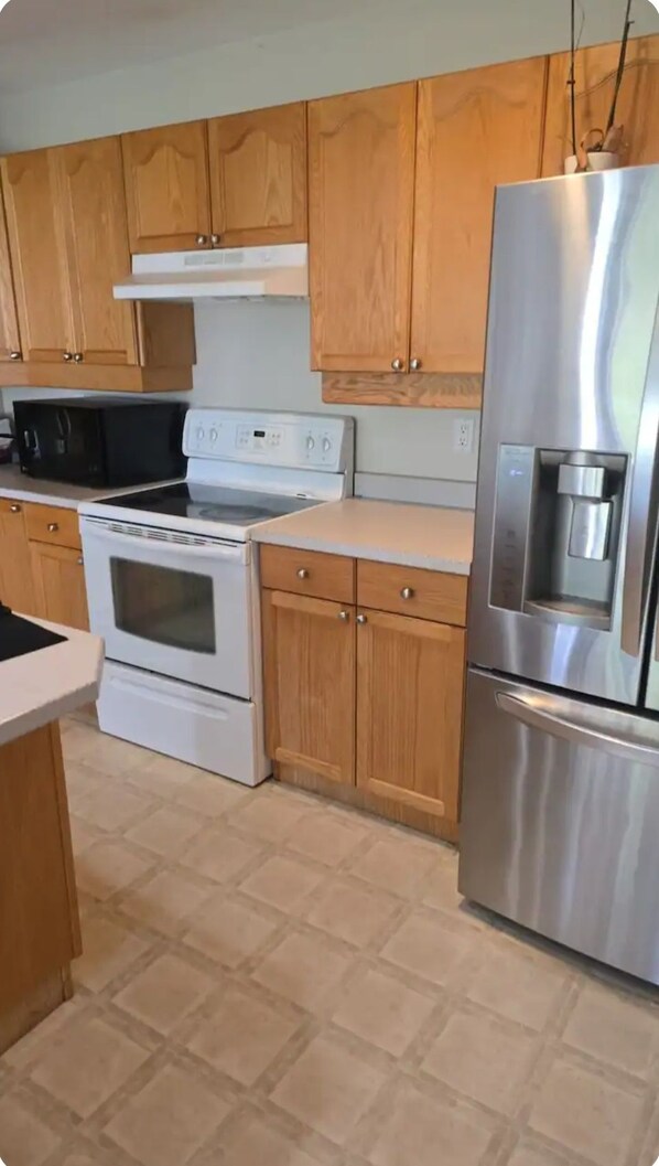 A kitchen with wooden cabinets, a stainless steel refrigerator, a microwave, a stove, and a water dispenser.