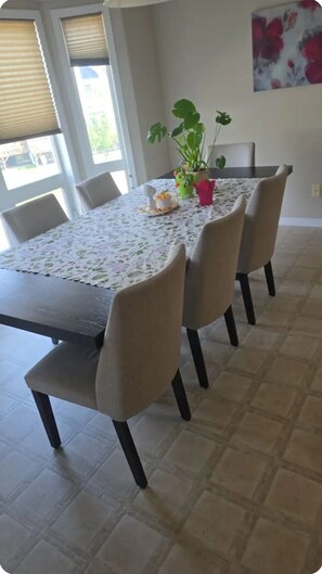 A dining table with a floral tablecloth, four chairs, a potted plant, and a cake on the table.