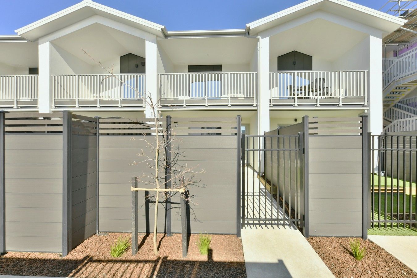 A modern building with a flat roof, a balcony on the upper floor, and a gated entrance.