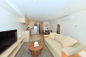 A modern living room with a flat-screen TV, a beige sofa, and a wooden coffee table. - Stylish 1 Bedroom Apartment with Private Yard (Christchurch)