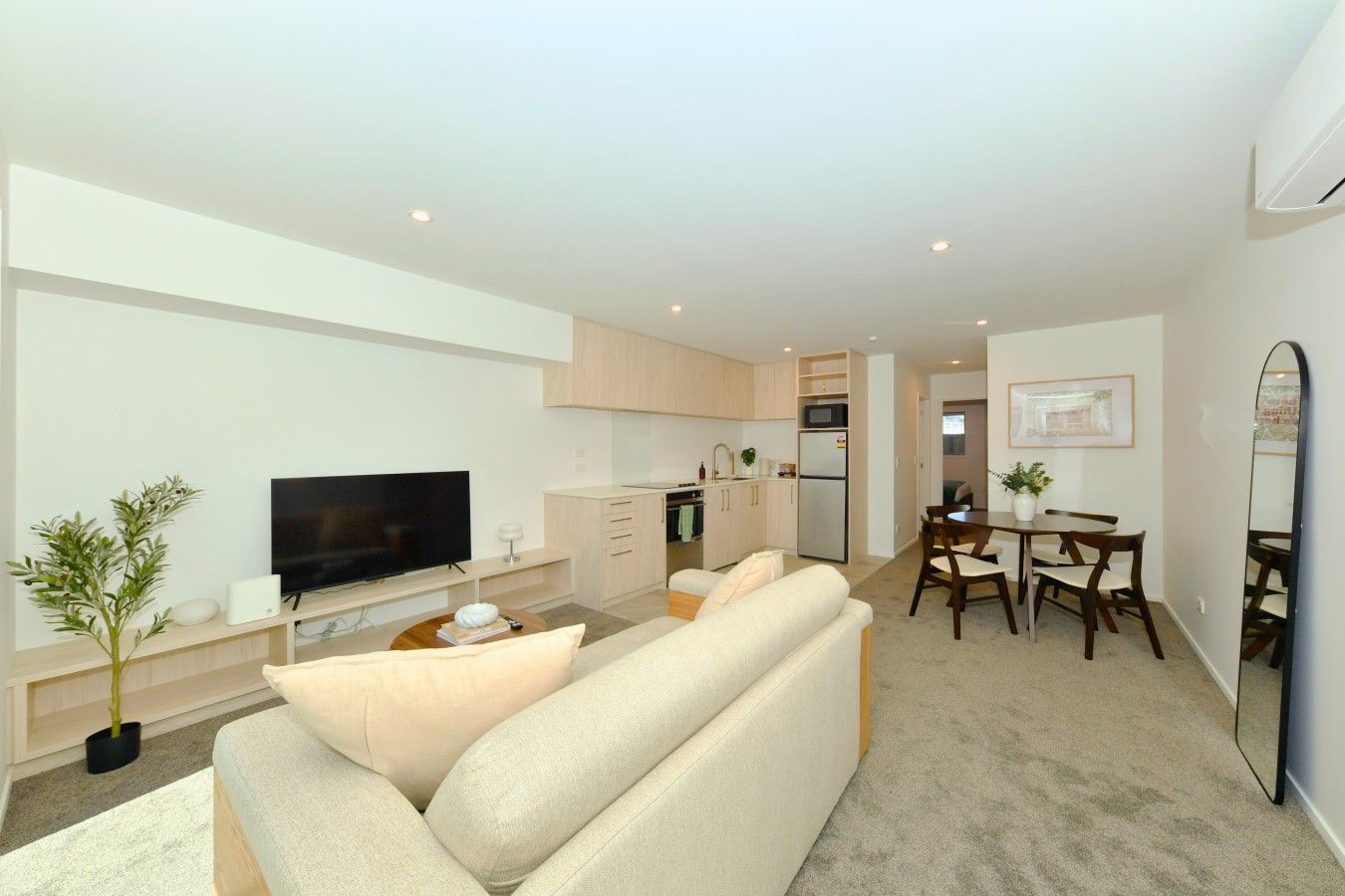 A modern living room with a flat-screen TV, a sofa, a coffee table, and a dining area with a table and chairs.