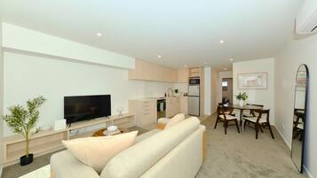 A modern living room with a flat-screen TV, a sofa, a coffee table, and a dining area with a table and chairs.