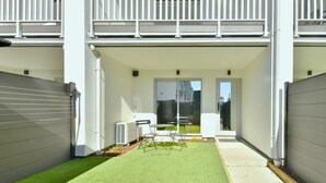 Un edificio moderno con un patio cubierto que incluye césped artificial, un conjunto de asientos y vistas del entorno.