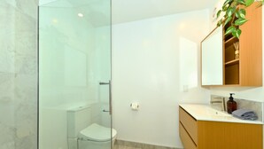 Un baño moderno con cabina de ducha de vidrio, inodoro, lavamanos con tocador de madera y espejo sobre el tocador.