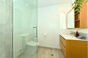 A modern bathroom with a glass shower enclosure, a toilet, a sink with a wooden vanity, and a mirror above the vanity. - Stylish 1 Bedroom Apartment with Private Yard (Christchurch)