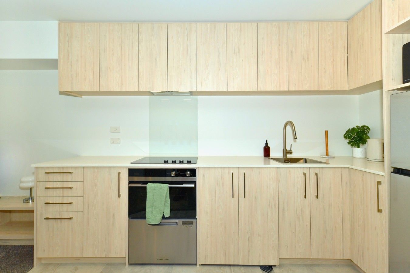 A modern kitchen with light wood cabinetry, a stainless steel oven, and a built-in dishwasher.