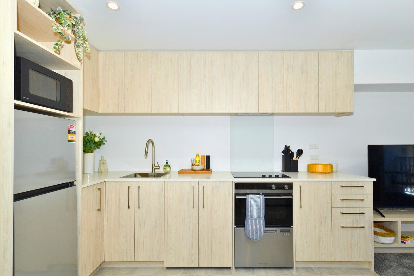 A modern kitchen with light wood cabinetry, a stainless steel refrigerator, a built-in oven, and a microwave.
