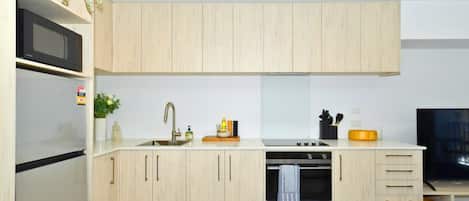 A modern kitchen with light wood cabinetry, a stainless steel refrigerator, a built-in oven, and a microwave.