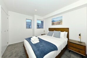 A hotel room with a large bed, a nightstand, a lamp, and a painting on the wall. - Modern 1 Bedroom Apartment with Private Balcony (Christchurch)