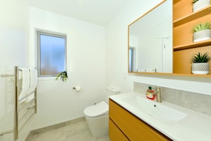 Un baño moderno con inodoro, lavamanos y una ventana con planta.